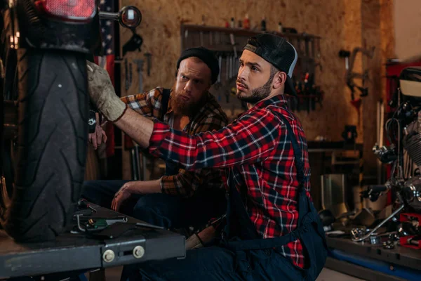 Handsome mechanics repairing motorcycle together at garage — Stock Photo