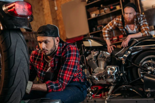 Focused mechanic fixing motorcycle while his colleague standing on background — Stock Photo