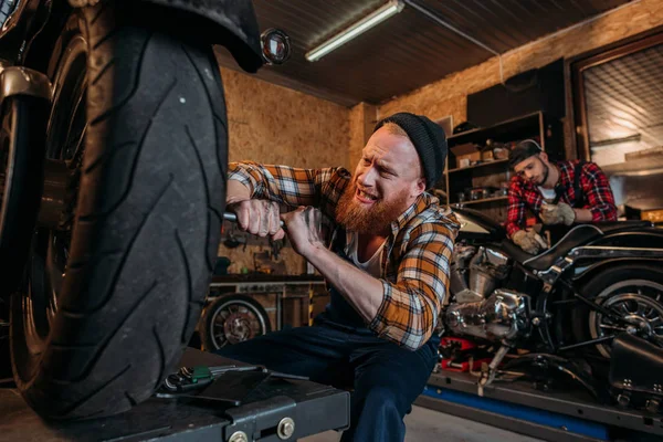 Meccanico teso fissaggio moto mentre il suo collega di lavoro su sfondo — Foto stock