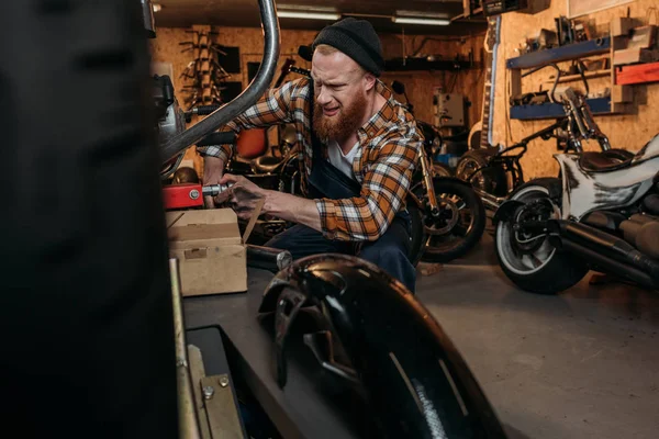 Travailleur émotionnel de station de réparation de vélo essayant de réparer le vélo au garage — Photo de stock