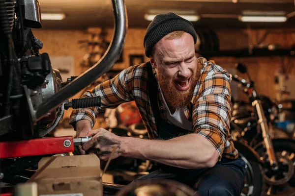 Trabalhador da estação de reparação tentando consertar bicicleta na garagem e gritando ao colega — Fotografia de Stock