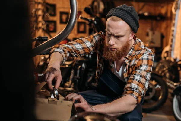 Beau travailleur de station de réparation de vélo essayant de trouver des détails dans la boîte au garage — Photo de stock