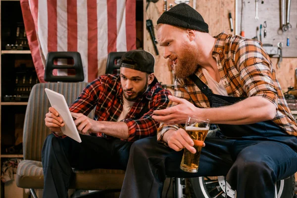 Mecânica beber cerveja e usar tablet juntos na garagem — Fotografia de Stock