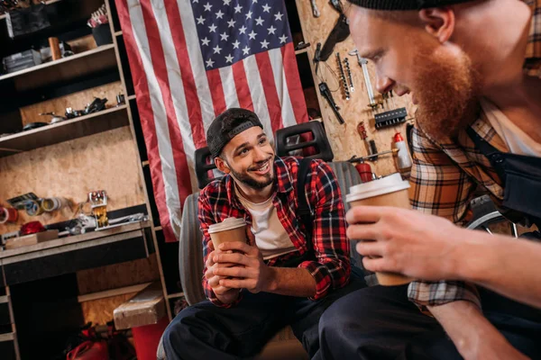 Mecánicos guapos beber café de tazas desechables en el descanso en el garaje - foto de stock