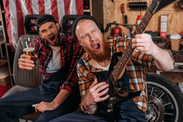 Mecánicos borrachos tocando la guitarra y bebiendo cerveza en el garaje — Stock Photo