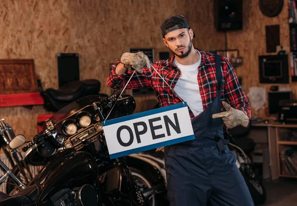 Handsome bike repair station worker pointing at open signboard at garage — Stock Photo