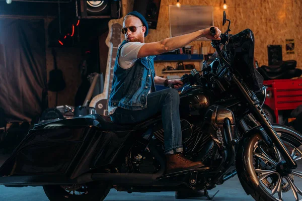 Schöner junger Mann sitzt auf Motorrad in Garage — Stockfoto