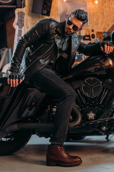 Joven guapo en ropa elegante sentado en motocicleta en el garaje - foto de stock