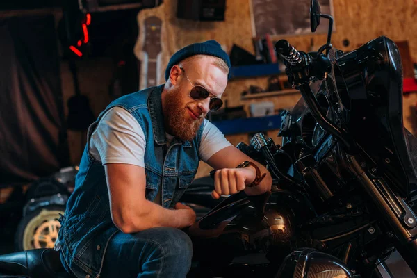 Junger Mann schaut auf Uhr, während er auf Fahrrad in Garage sitzt — Stockfoto