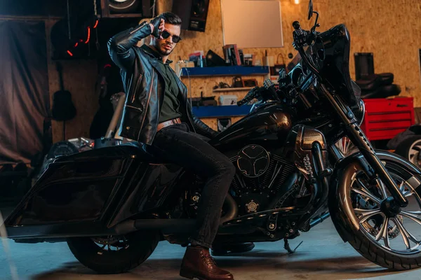 Schöner junger Mann mit Sonnenbrille sitzt auf Fahrrad in Garage — Stockfoto