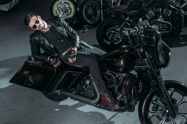 High angle view of handsome young man in leather jacket lying on bike at garage — Stock Photo