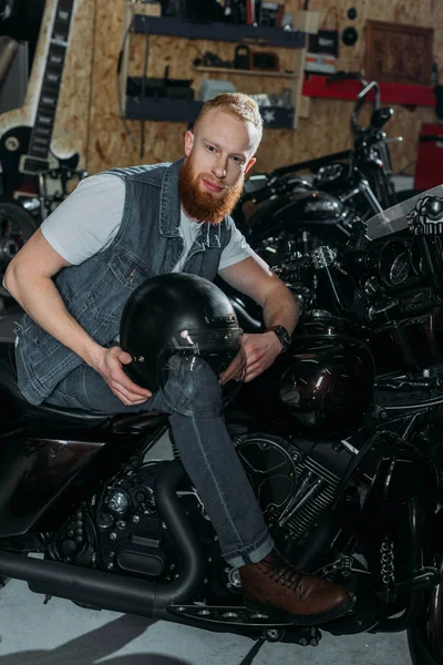 Jovem sentado em moto com capacete na garagem — Fotografia de Stock