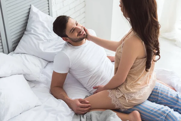 Vista parcial de un joven sonriente mirando a su novia en la cama - foto de stock