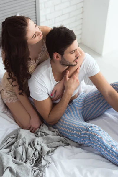 Молода пара в піжамі сидить на ліжку вдома — стокове фото