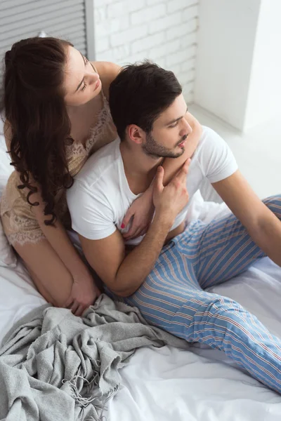 Pareja joven en pijama sentada en la cama en casa - foto de stock