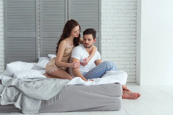 Junge Frau im Schlafanzug umarmt Freund zu Hause auf dem Bett — Stockfoto