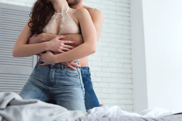 Обрезанный снимок молодой соблазнительной пары в джинсах на кровати дома — стоковое фото
