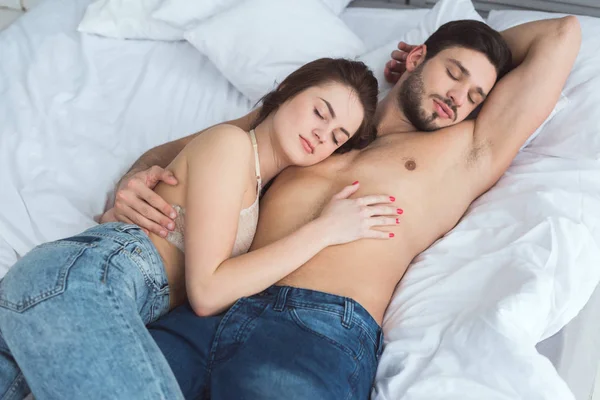 Young couple in jeans sleeping on bed together at home — Stock Photo