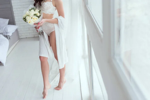 Обрізаний знімок жінки в нижній білизні з букетом троянд, що стоїть біля вікна — стокове фото