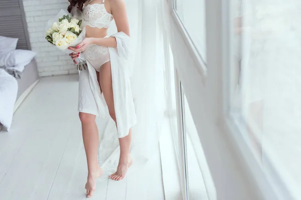 Tiro recortado de mujer en ropa interior con ramo de rosas de pie en la ventana - foto de stock