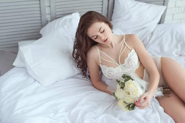 Femme sexy en sous-vêtements blancs avec bouquet de roses reposant sur le lit — Photo de stock