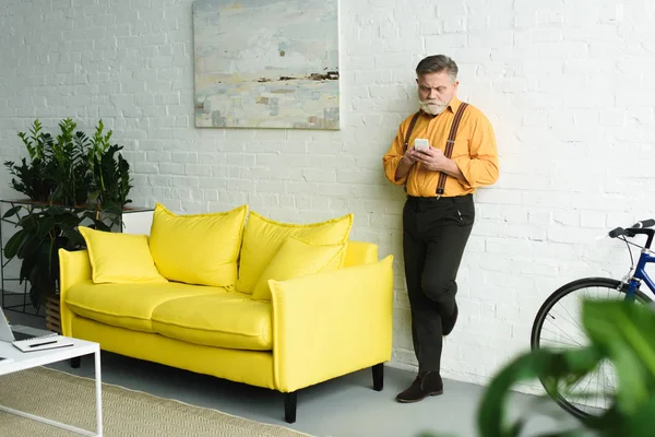 Homem sênior barbudo elegante usando smartphone em casa — Fotografia de Stock