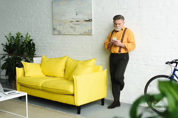 Hombre mayor barbudo con estilo utilizando el teléfono inteligente en casa — Stock Photo