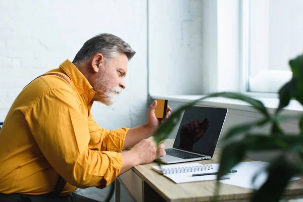 Bearded senior man holding credit card and using laptop at home — Stock Photo