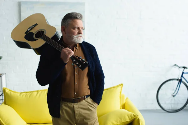 Confident senior man holding guitar and looking away at home — Stock Photo