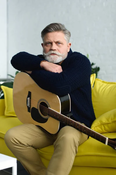 Guapo barbudo hombre mayor sentado con la guitarra y mirando a la cámara - foto de stock