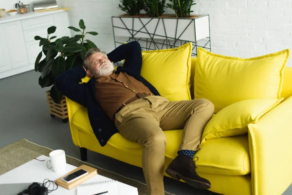 Cher homme âgé barbu couché sur le canapé avec les mains derrière la tête et levant les yeux — Photo de stock