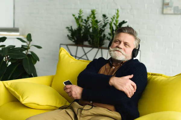 Heureux homme âgé dans écouteurs écouter de la musique avec smartphone à la maison — Photo de stock