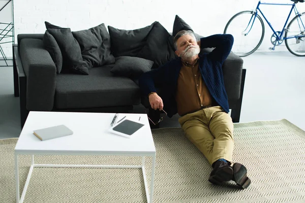 Homme barbu détendu assis sur le tapis et penché sur le canapé à la maison — Photo de stock