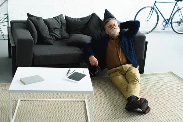 Relaxed bearded man sitting on carpet and leaning at sofa at home — Stock Photo