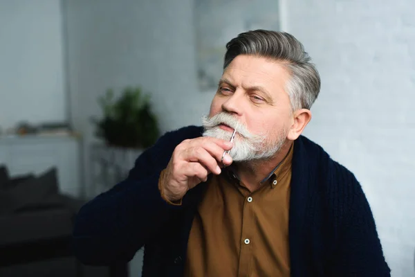 Bonito homem sênior cortando bigode com tesoura em casa — Fotografia de Stock