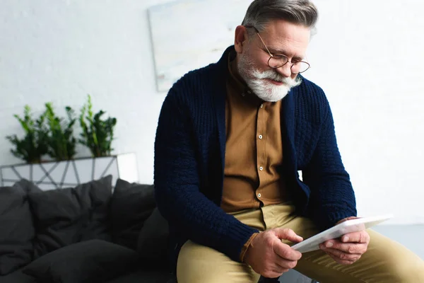 Uomo anziano barbuto sorridente in occhiali da vista utilizzando tablet digitale a casa — Foto stock