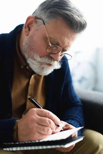 Close-up view of concentrated senior man in eyeglasses writing in notebook — Stock Photo