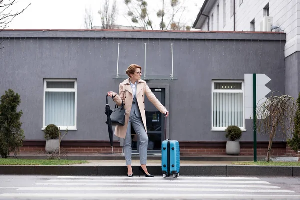 Mujer de negocios con maleta y paraguas esperando taxi en la calle - foto de stock