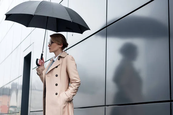 Vista lateral de empresária em casaco elegante com guarda-chuva na rua — Fotografia de Stock