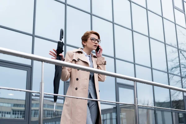 Geschäftsfrau mit Regenschirm telefoniert auf Straße mit Smartphone — Stockfoto
