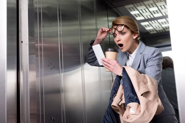 Portrait of shocked businesswoman in suit with smartphone in elevator — Stock Photo