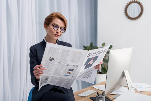 Portrait of businesswoman in eyeglasses reading newspaper at workplace in office — Stock Photo