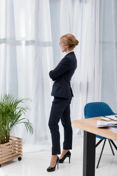 Боковой вид застенчивой бизнесвумен в костюме, выглядывающей из окна офиса — стоковое фото
