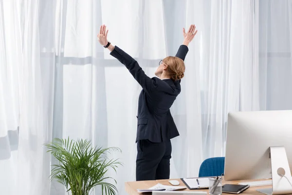 Side view of businesswoman in suit stretching and looking out window in office — Stock Photo