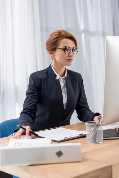 Mujer de negocios enfocada que trabaja en el lugar de trabajo con documentos pantalla de computadora en la oficina - foto de stock