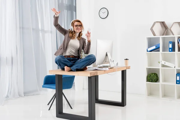 Businesswoman in headphones with smartphone listening music on table in office — Stock Photo