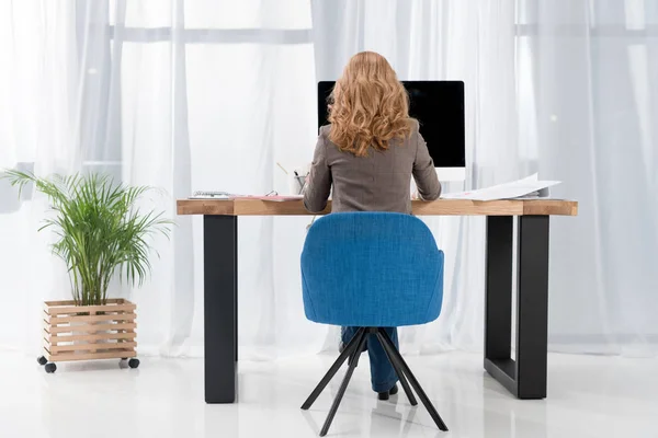 Назад вид деловой женщины, работающей на рабочем месте с компьютерным экраном в офисе — стоковое фото