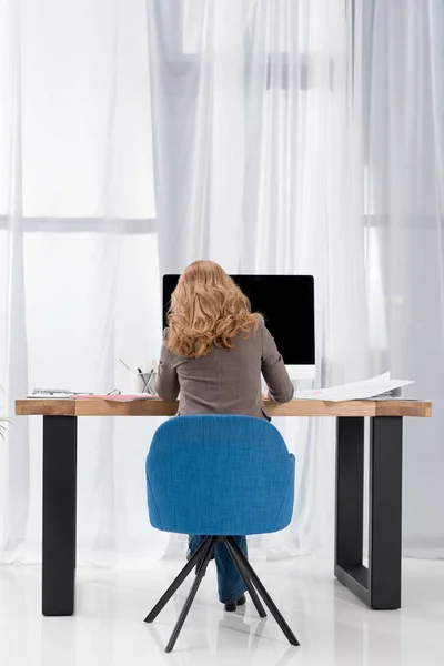 Вид ззаду бізнес-леді, що працює на робочому місці з екраном комп'ютера в офісі — стокове фото