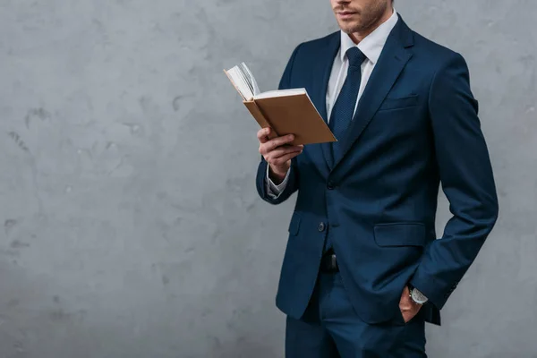 Cropped shot of businessman reading book in front of concrete wall — Stock Photo