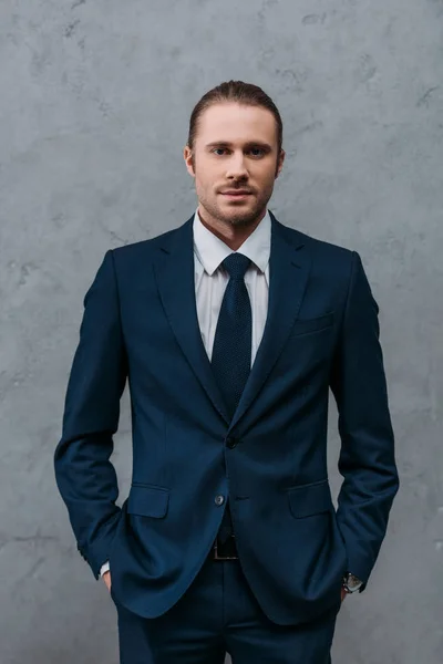 Joven hombre de negocios guapo en traje elegante delante de la pared de hormigón - foto de stock